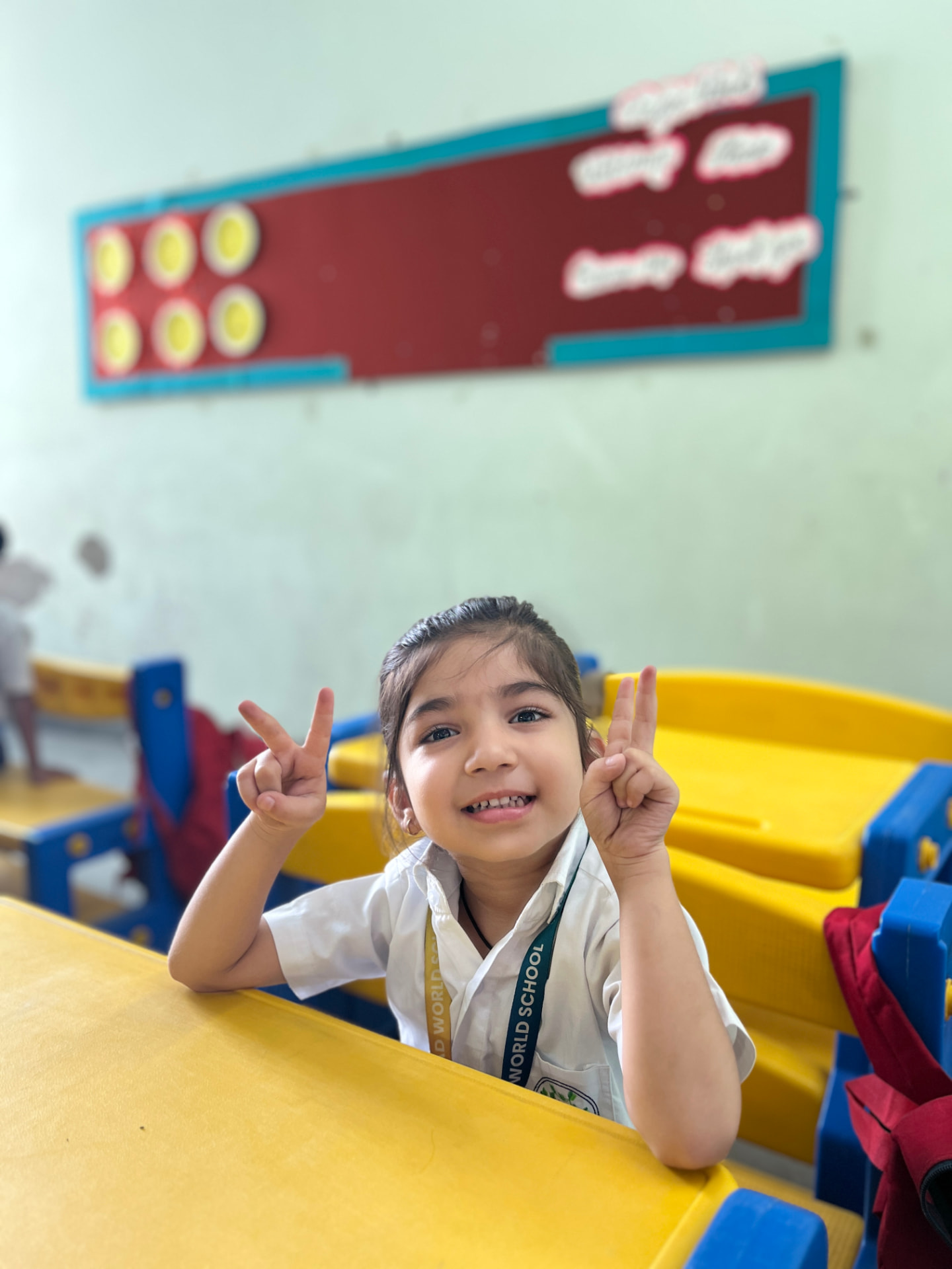 A smiling student showing a victory sign at her classroom desk