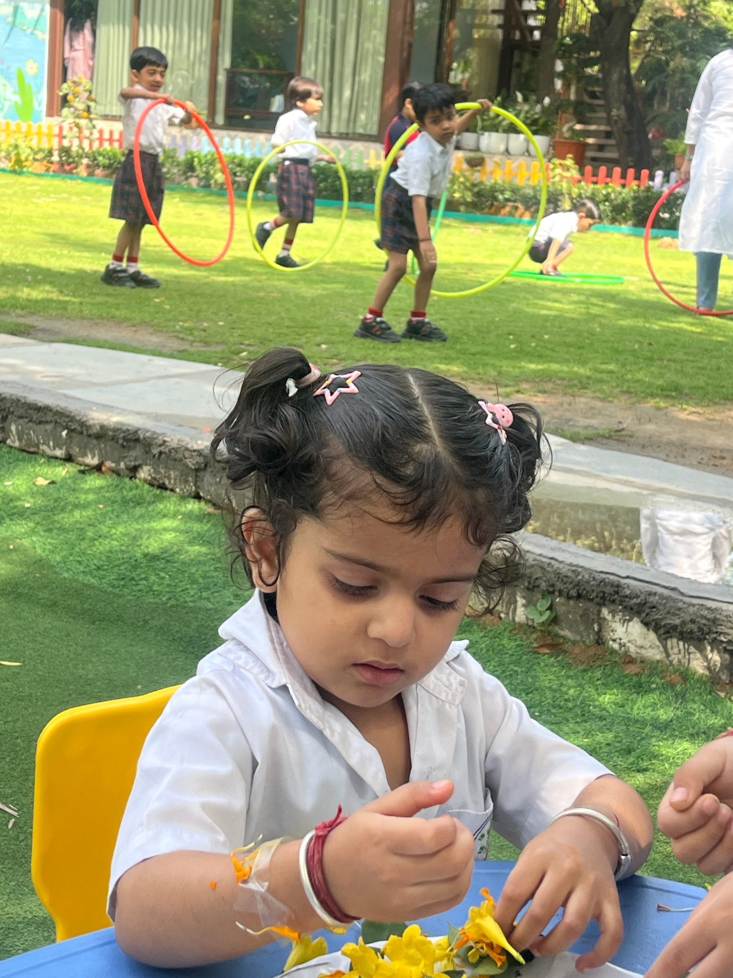 Children doing flower craft on the lawn while friends play with hoops