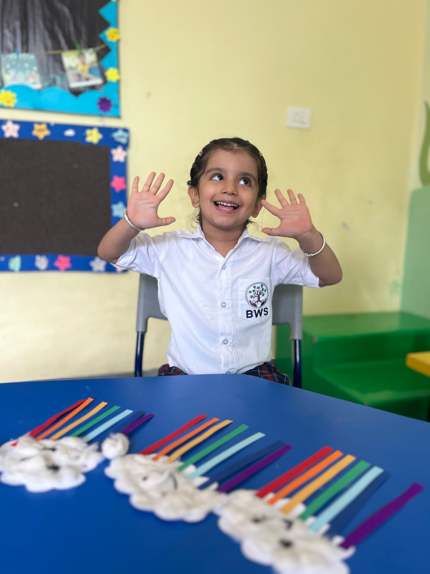 A delighted preschooler with her rainbow craft in class