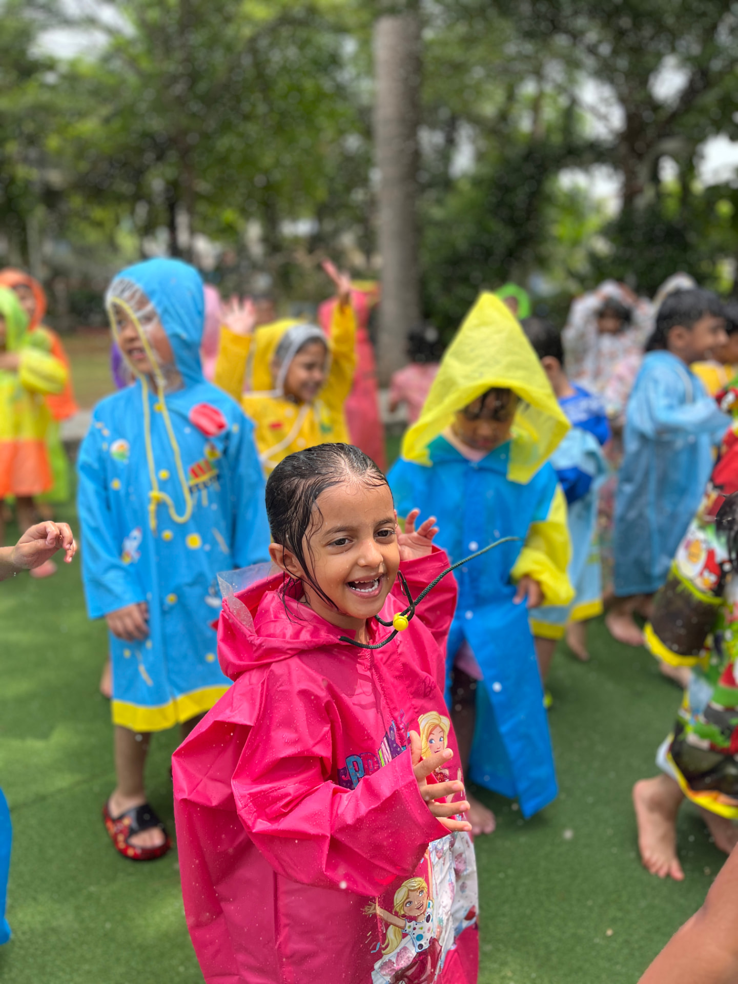 Children in colourful raincoats enjoying rain dance in the garden